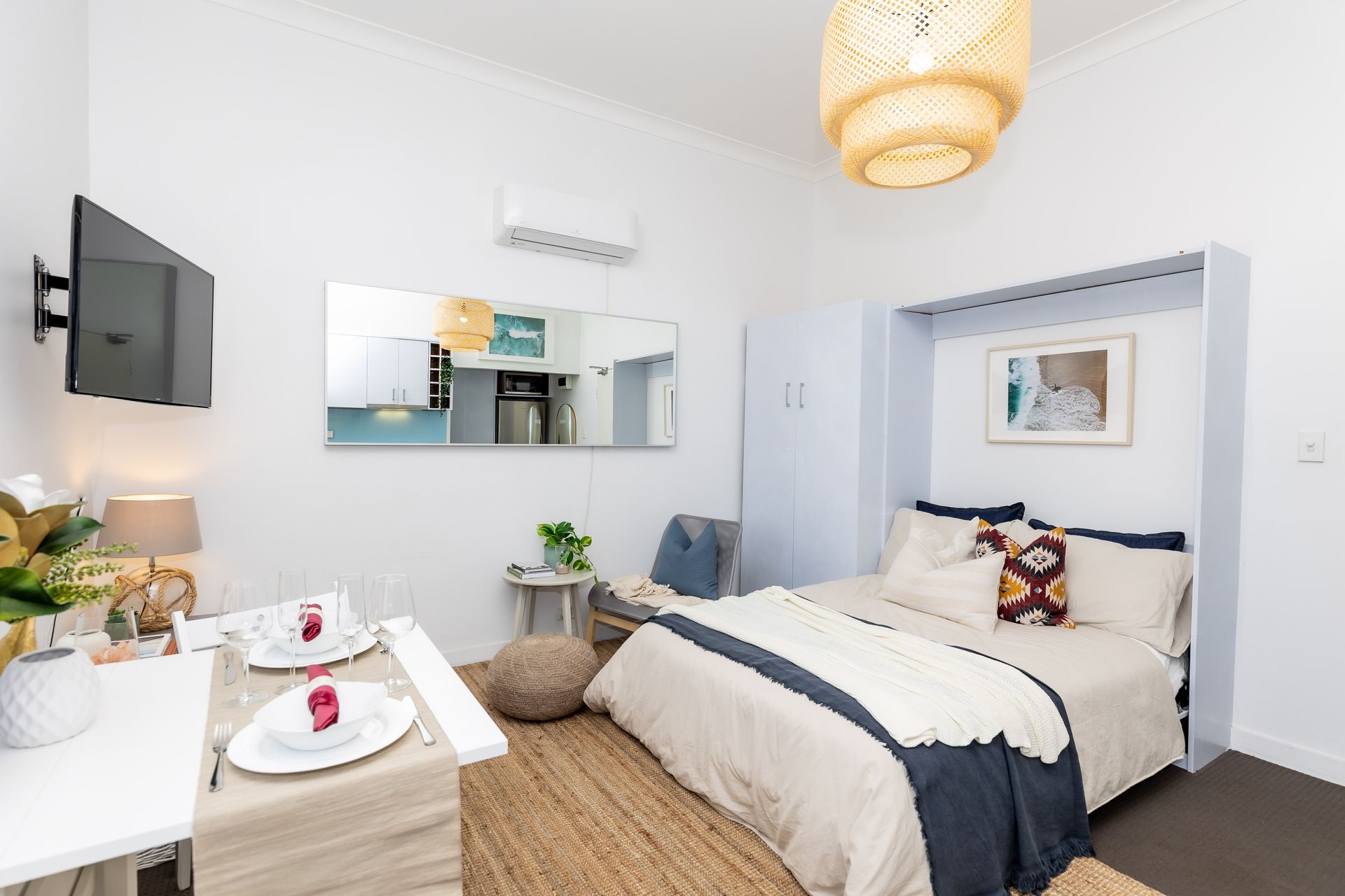 Bright bedroom with a neatly made bed, wall mirror, hanging lamp, and white decor accents