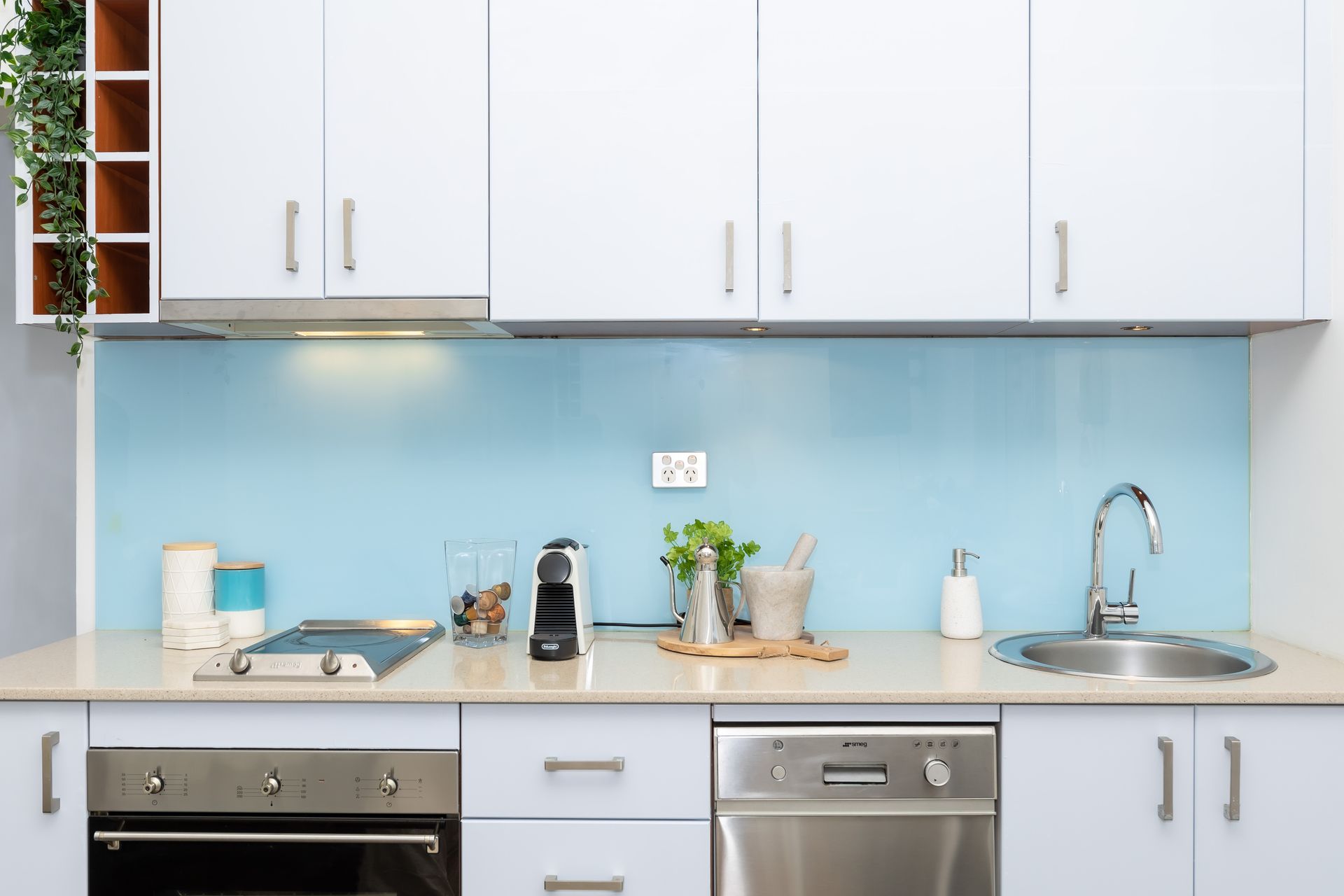 Modern white kitchen with blue backsplash, countertop items, sink, stove, and dishwasher