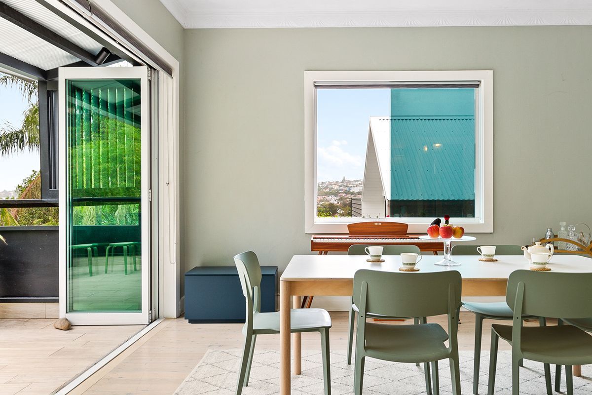 Bright dining room with open glass door, white table, and green chairs overlooking a balcony and city view