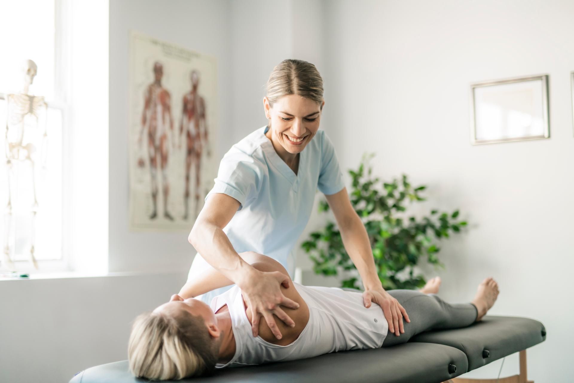 Eine Frau liegt auf einem Tisch und wird von einer Physiotherapeutin massiert.