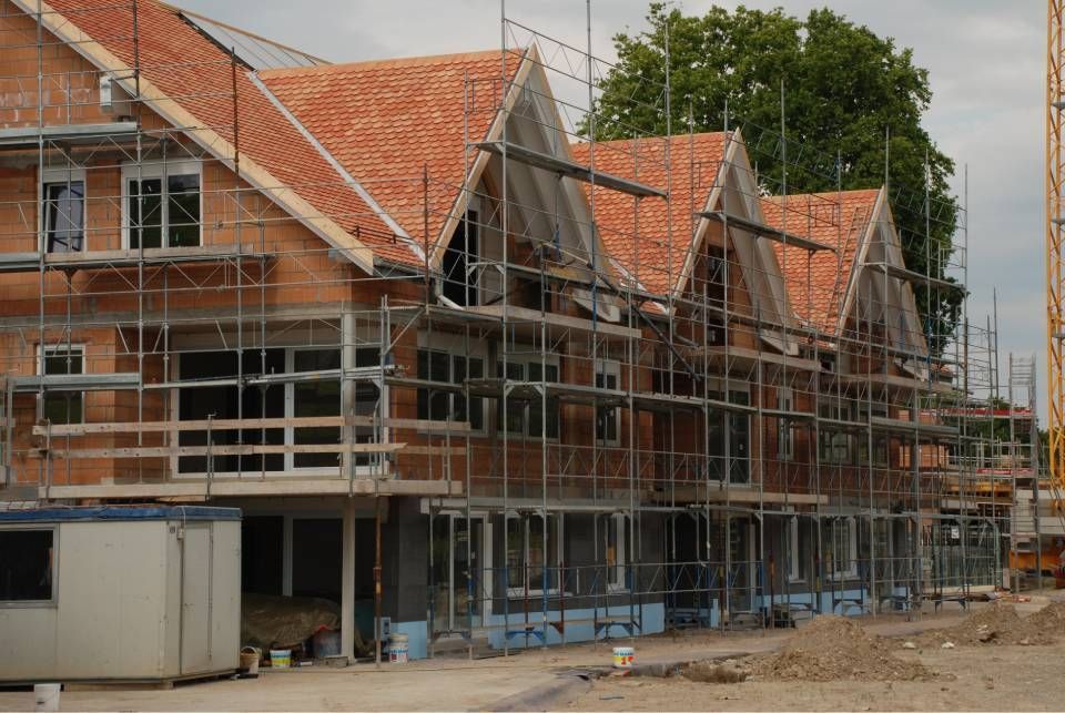 Bâtiment en construction ; façade en briques, toit de tuiles rouges, échafaudages.