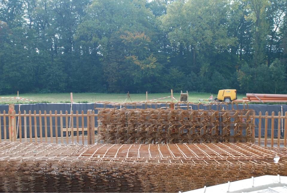 Chantier de construction avec des plaques d'armature au premier plan, une clôture en bois et des arbres à l'arrière-plan.
