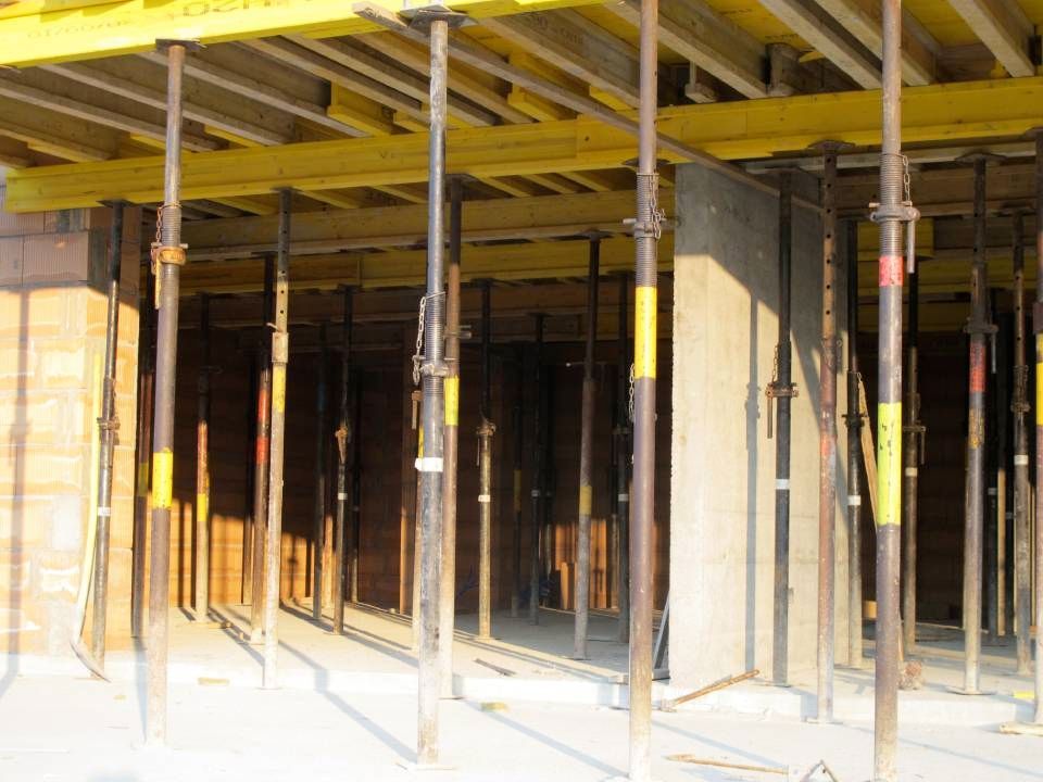 Chantier de construction avec coffrages en bois et supports métalliques soutenant un plafond.