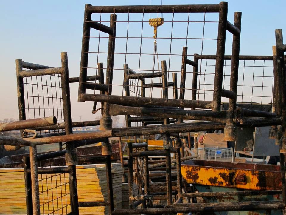 Sculpture en ferraille avec un crochet jaune suspendu à une grue, sur fond de ciel bleu.