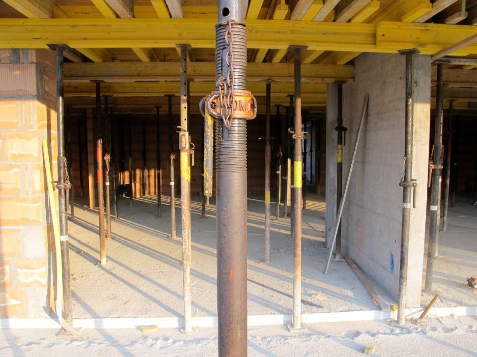 Chantier : sol en béton avec des colonnes de soutien supportant des poutres en bois.