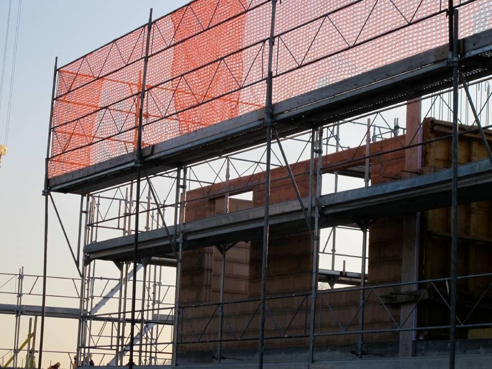 Chantier de construction avec échafaudages et filets de sécurité orange sur un bâtiment en construction.