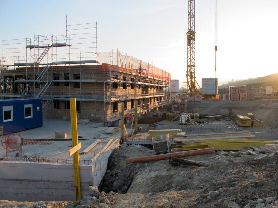 Chantier de construction avec bâtiment en construction, grue, échafaudages et matériaux ; en journée.