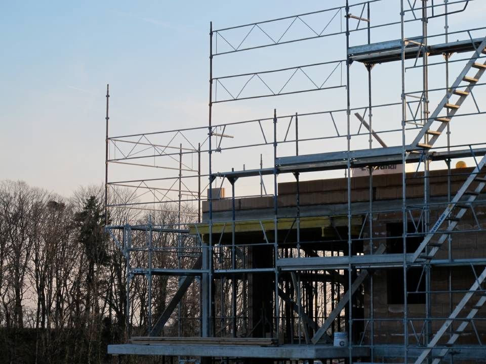 Échafaudages entourant un bâtiment en construction, vue extérieure avec des arbres et le ciel en arrière-plan.