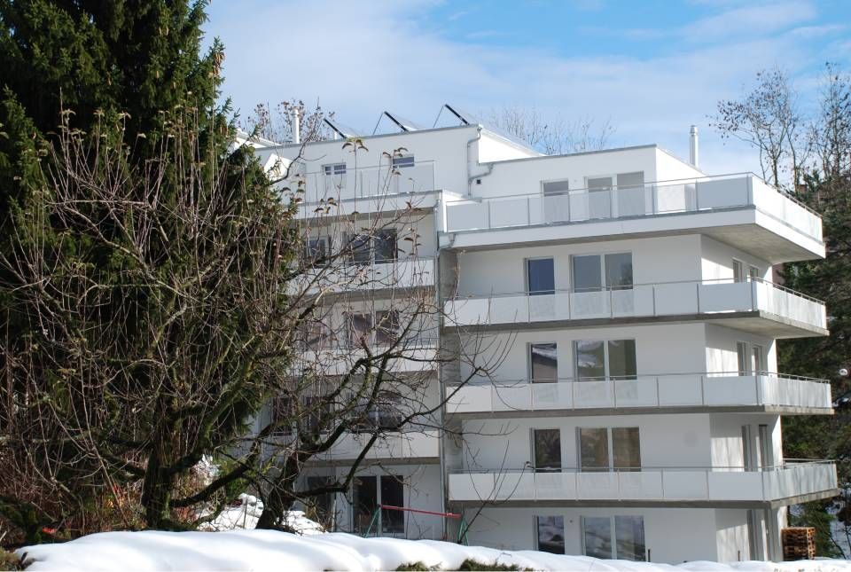 Immeuble d'appartements blanc à plusieurs étages avec balcons, neige au sol, arbre au premier plan.