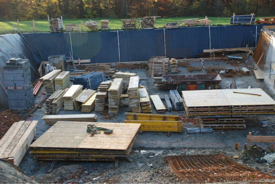 Chantier de construction avec des piles de bois, des outils et une clôture bleue.