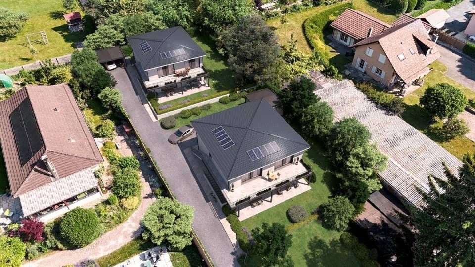 Vue aérienne de maisons aux toits gris foncé, aux jardins verdoyants et dotées d'une allée carrossable.