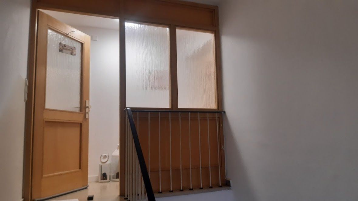 Eine Holztür und Milchglasplatten führen zu einem Treppenhaus mit einem Holzgeländer, das von sanftem Licht erhellt wird.