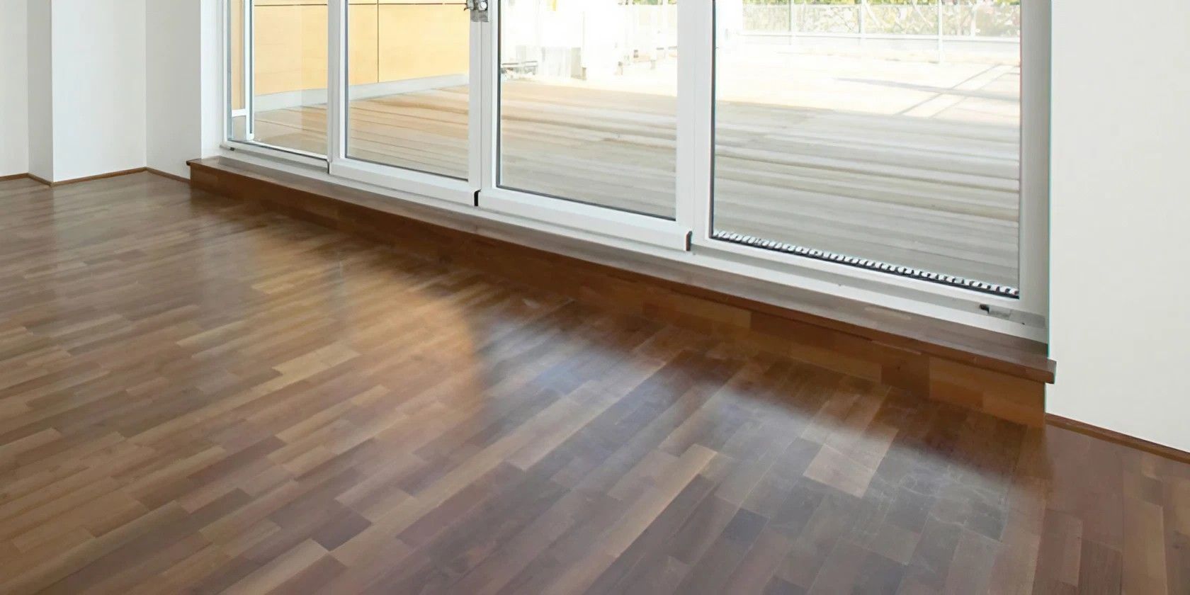 Holzboden in einem Raum mit großem Fenster. Der Raum ist gut beleuchtet, da das Sonnenlicht durch das Fenster fällt.