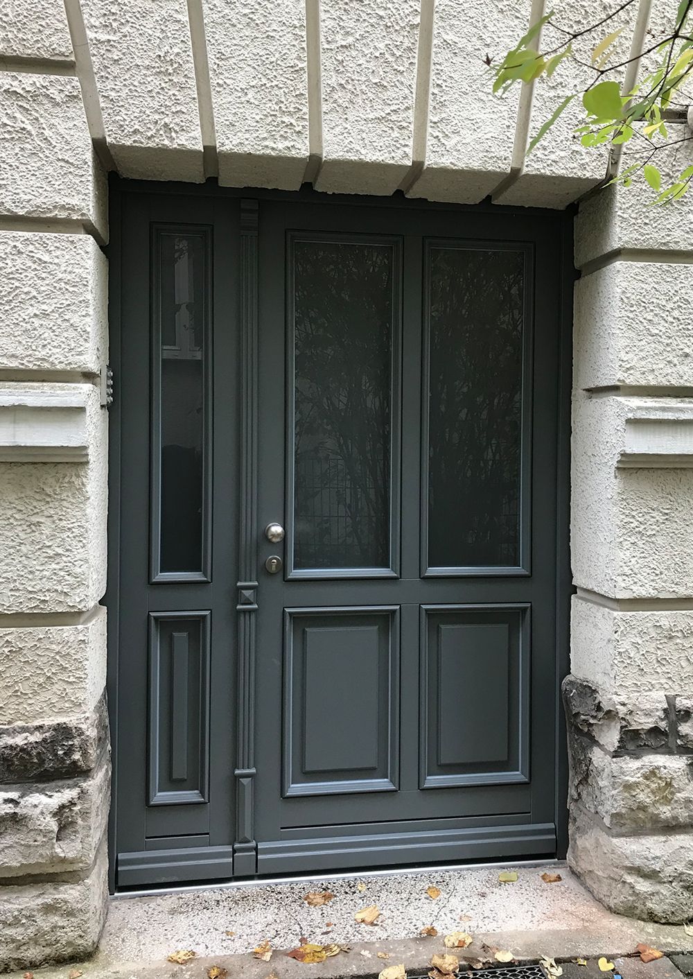 Graue Tür mit Glasplatten in einem Steinrahmen.