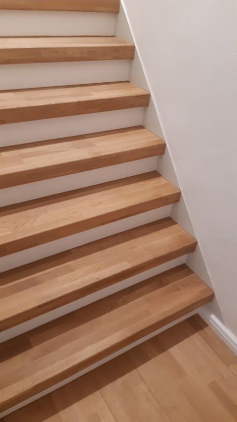 Holztreppe mit weißen Setzstufen vor einer weißen Wand, unten ist der Holzboden sichtbar.