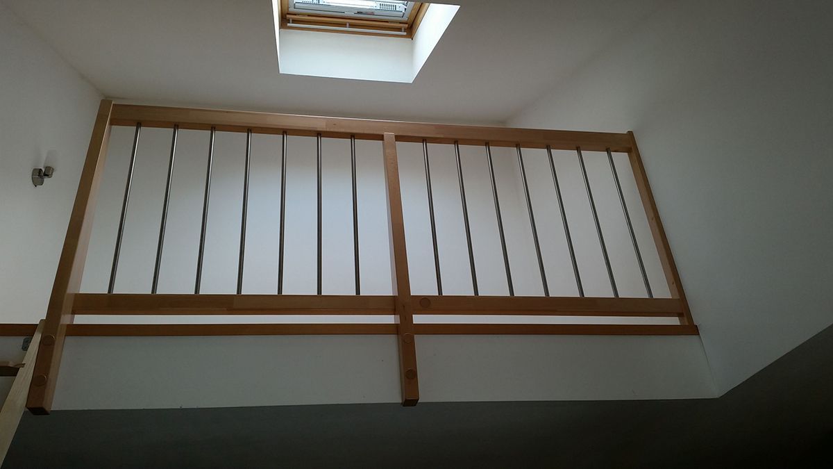 Innenansicht einer Treppe mit Holzgeländer, weißen Wänden und einem Oberlicht oben.