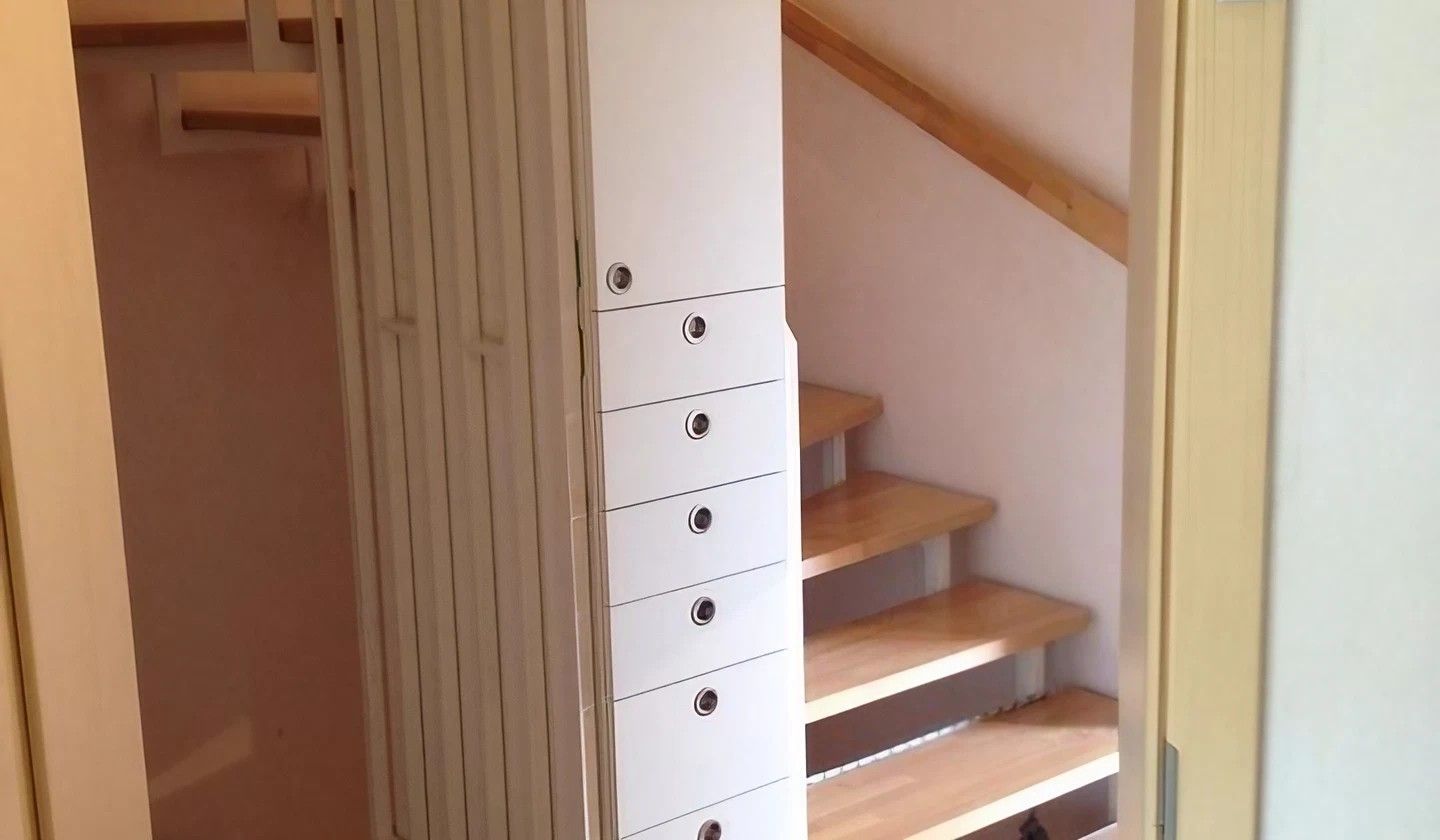 Weißer Schrank mit Schubladen neben der Holztreppe.