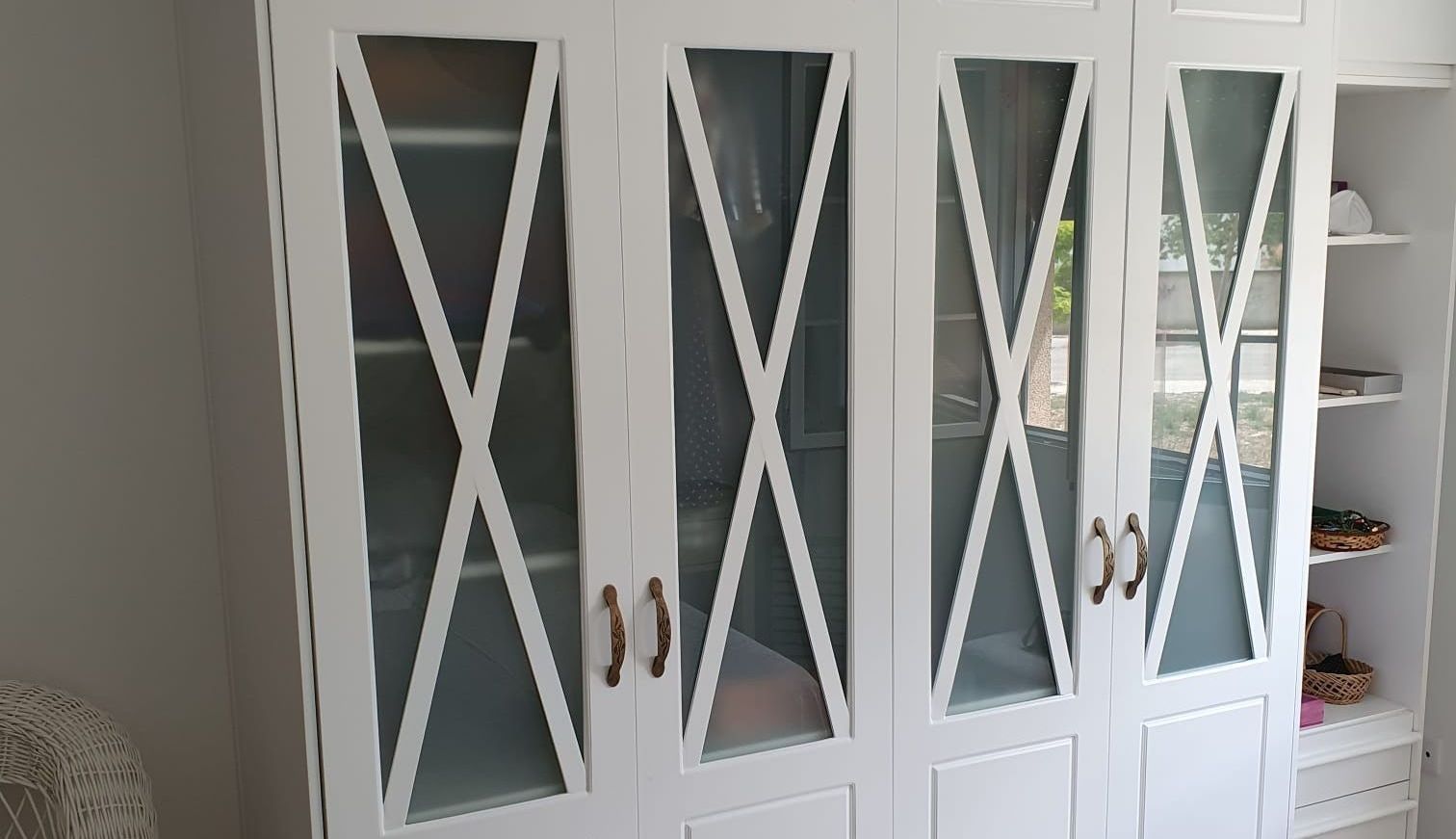 Un armario blanco con puertas de cristal y estantes en una habitación.