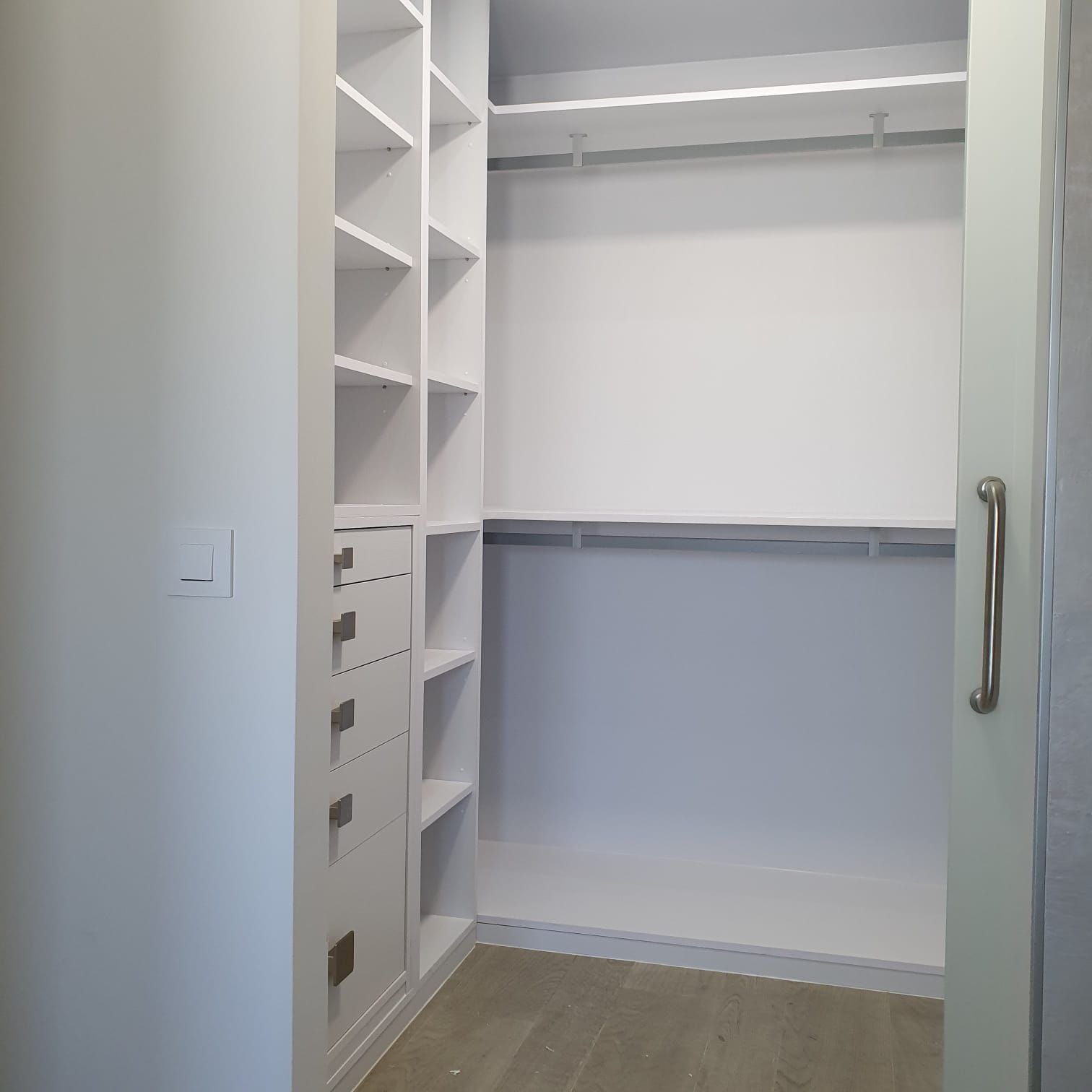 Un vestidor con muchos estantes y cajones y una puerta corrediza de vidrio.