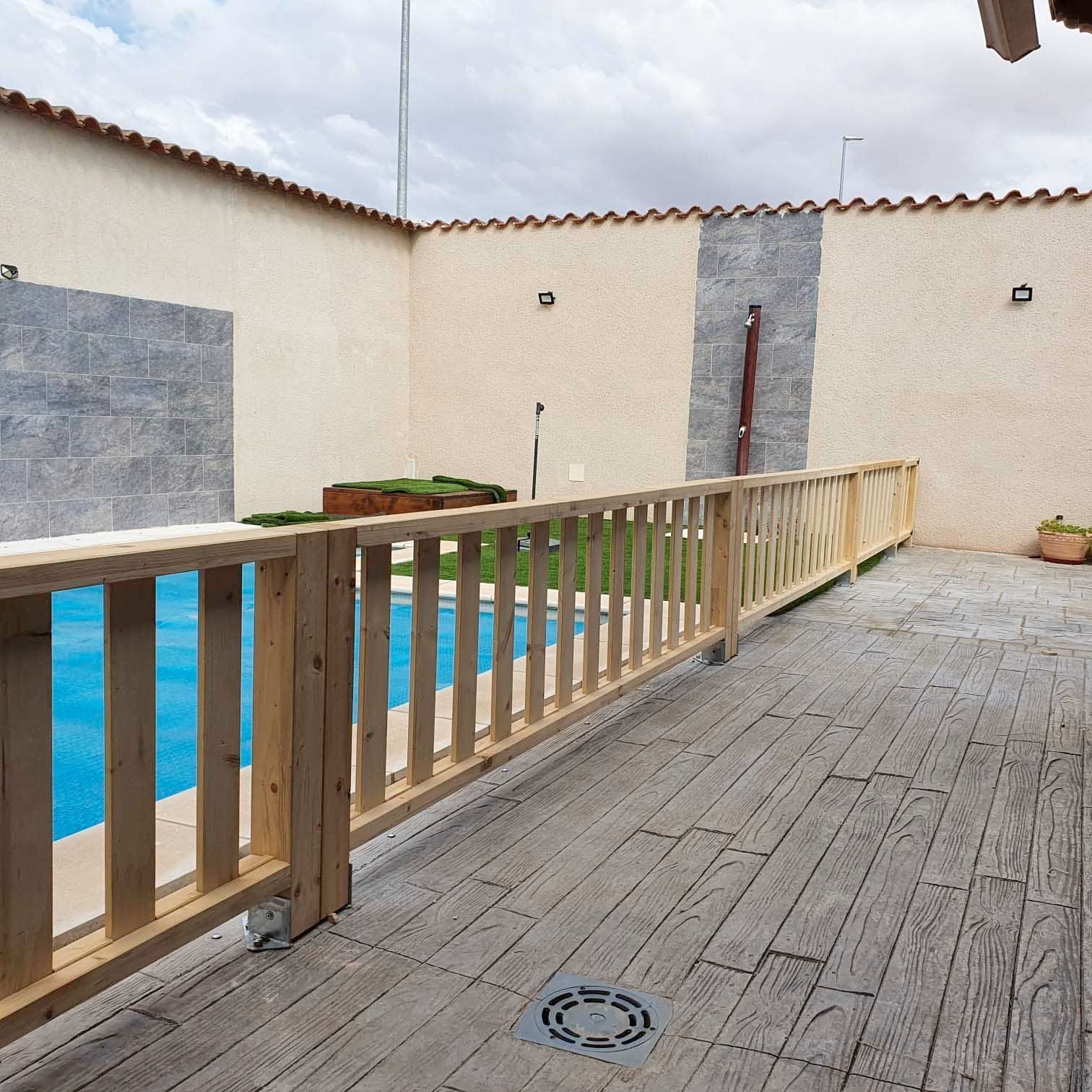 Una valla de madera rodea una piscina en un patio trasero.