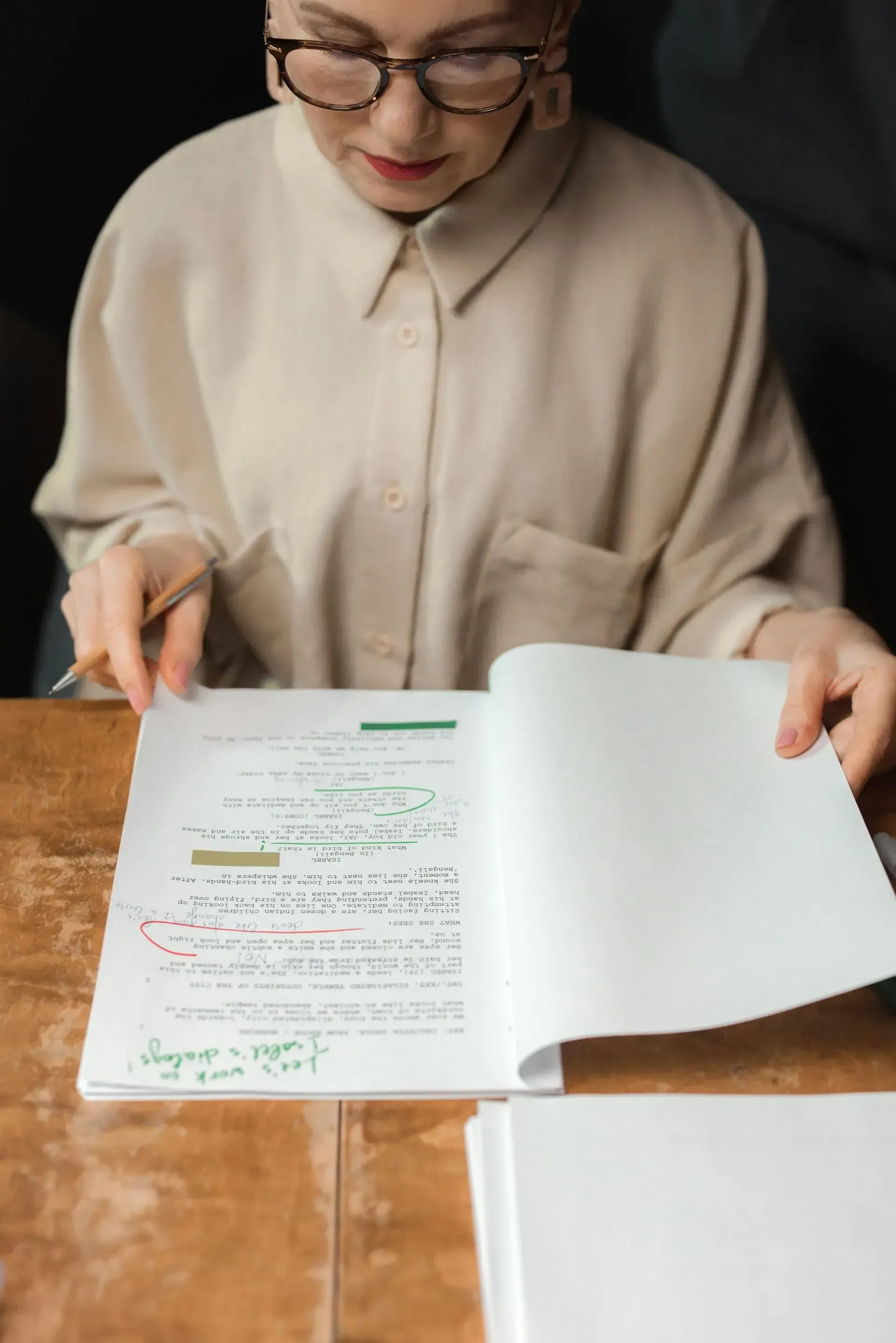 Una persona con gafas y camisa de color claro revisa un documento con notas manuscritas en una mesa de madera.