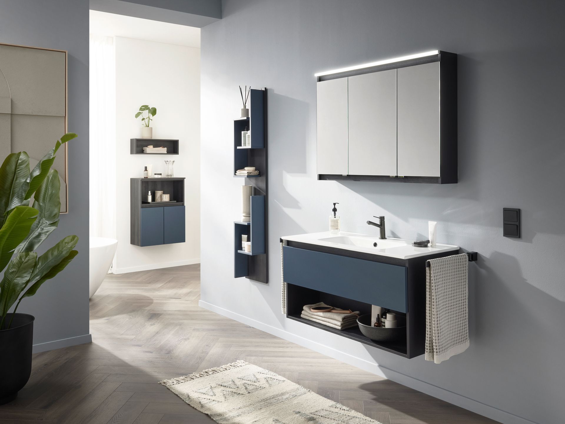 Badezimmer in hellgrauen Tönen mit Waschtisch, Spiegel und Pflanzen.