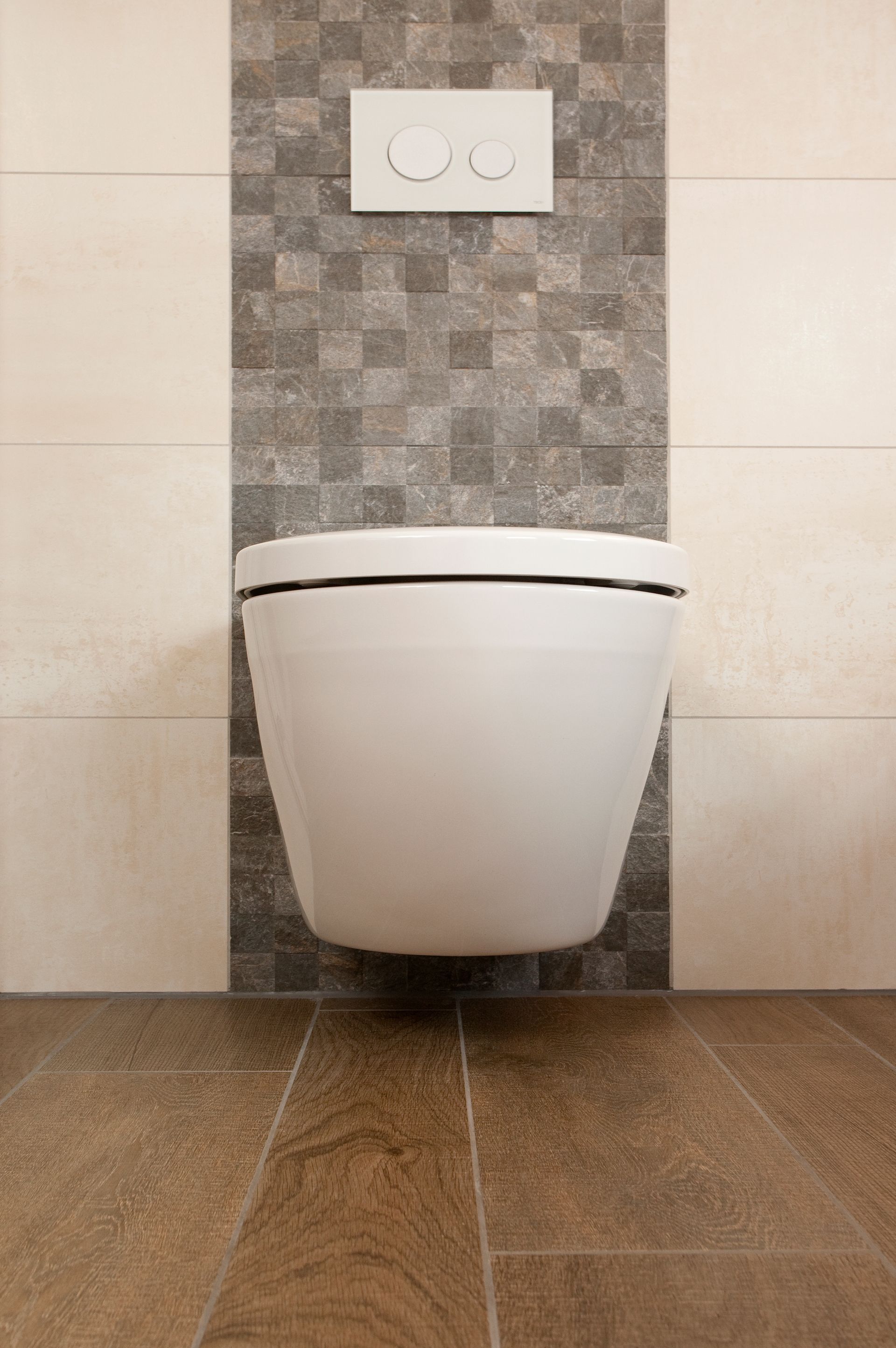 Hängendes WC mit vertikaler Akzentfliese in grauer Steinoptik.