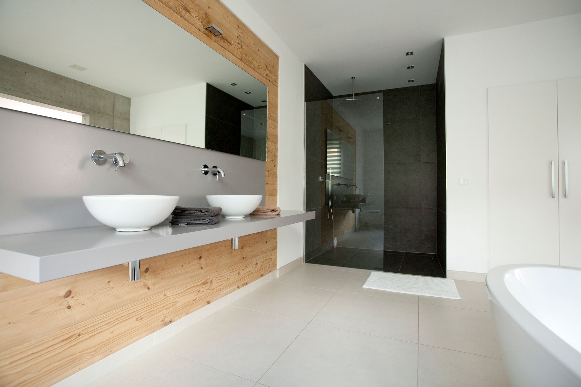 Waschbereich mit weißem Waschtisch, Holzdetails und großzügiger Dusche.