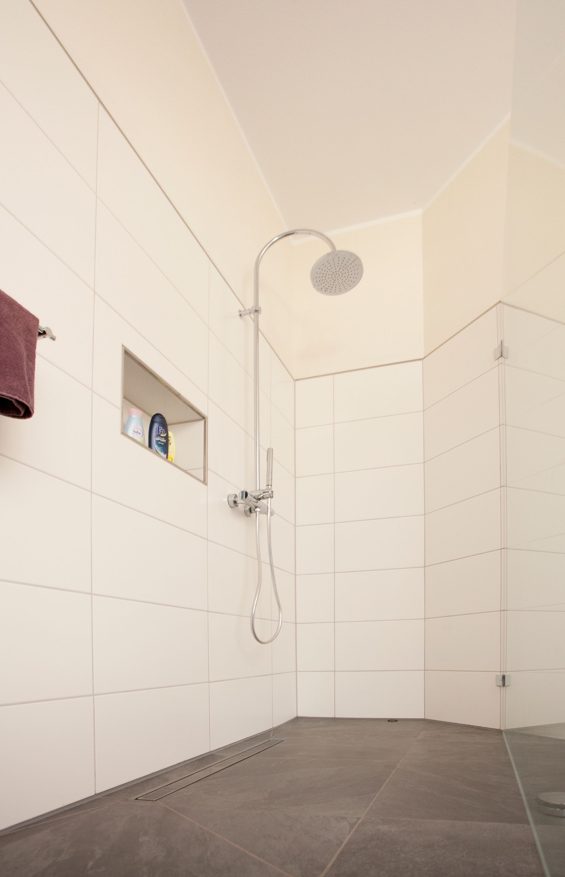 Ebenerdige Dusche mit weiß gefliester Wand und integrierter Duschrinne.