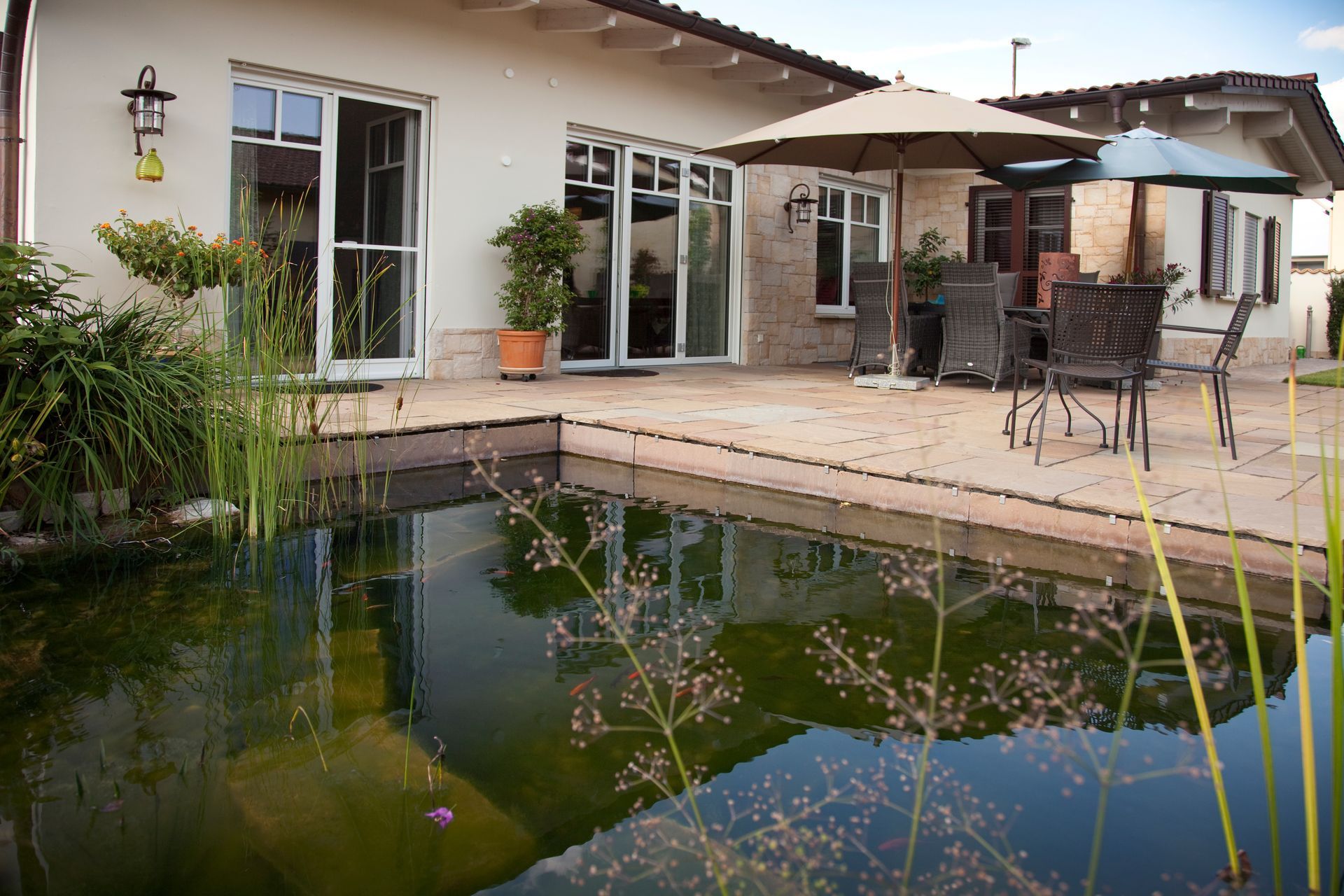 Barrierefreie Terrasse mit Sitzgruppe, angrenzend an einen Garten mit Wasserbecken.