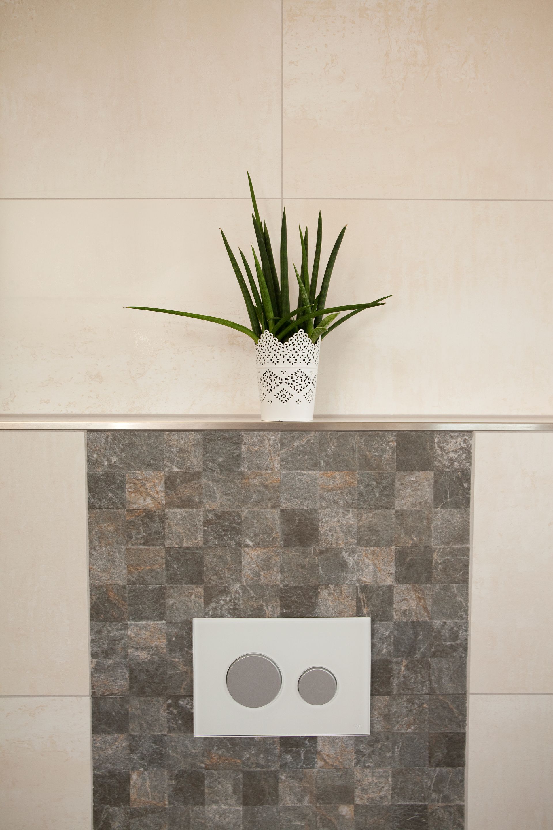 Wandgestaltung im Badezimmer mit grauen Mosaikfliesen und dekorativer Pflanze.