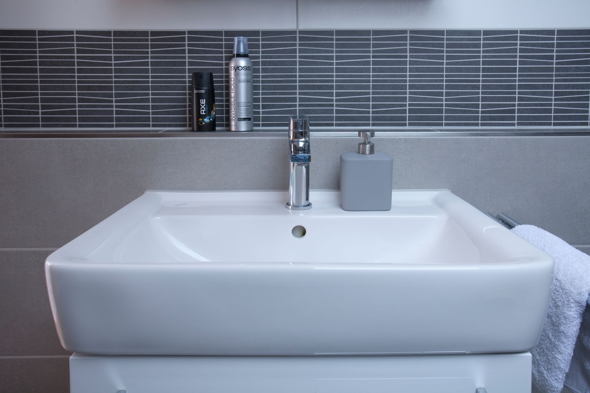 Waschbecken mit grauer Wandverkleidung und modernen Badaccessoires.