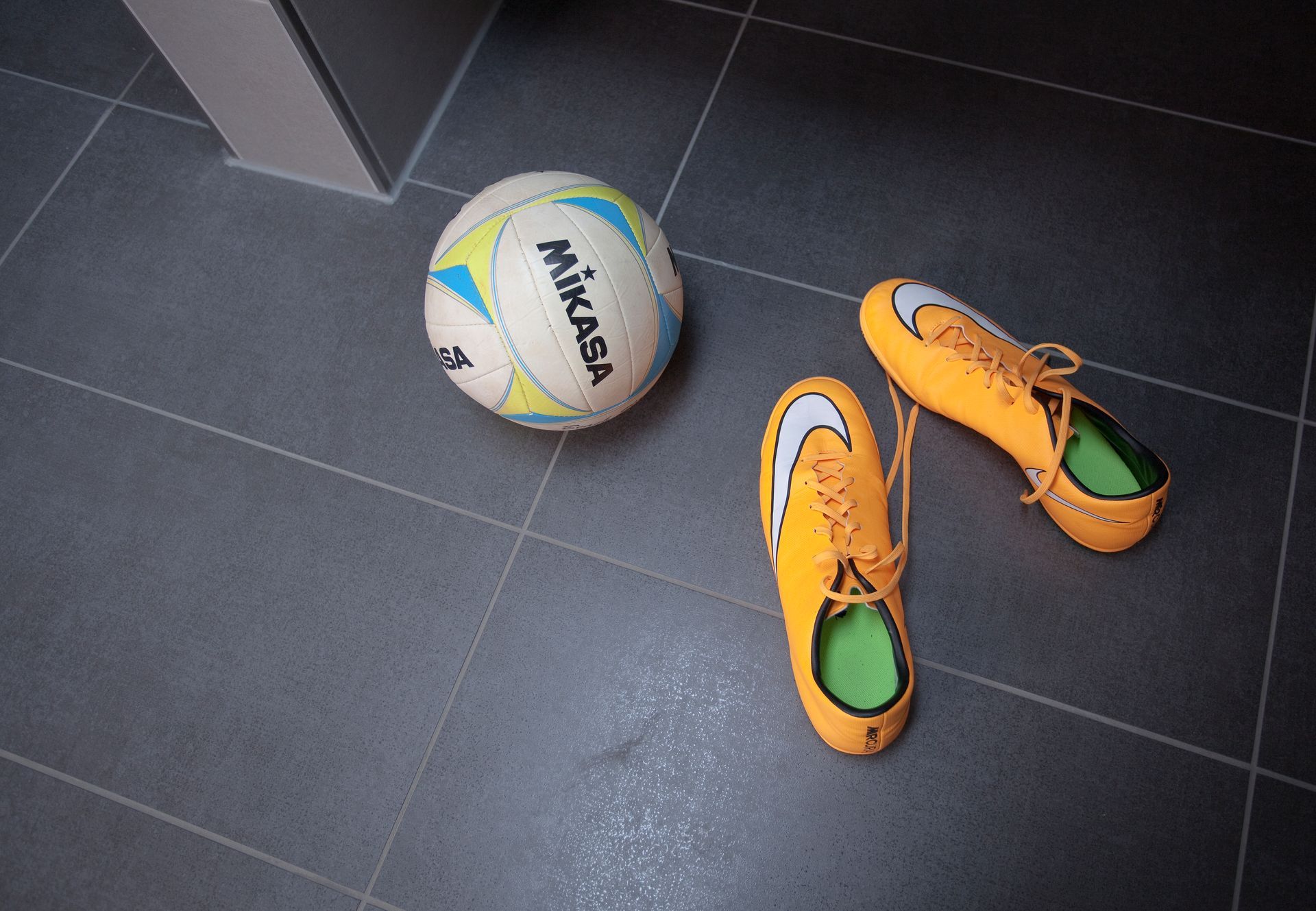 Detailaufnahme dunkler Bodenfliesen mit Volleyball und Sportschuhen.