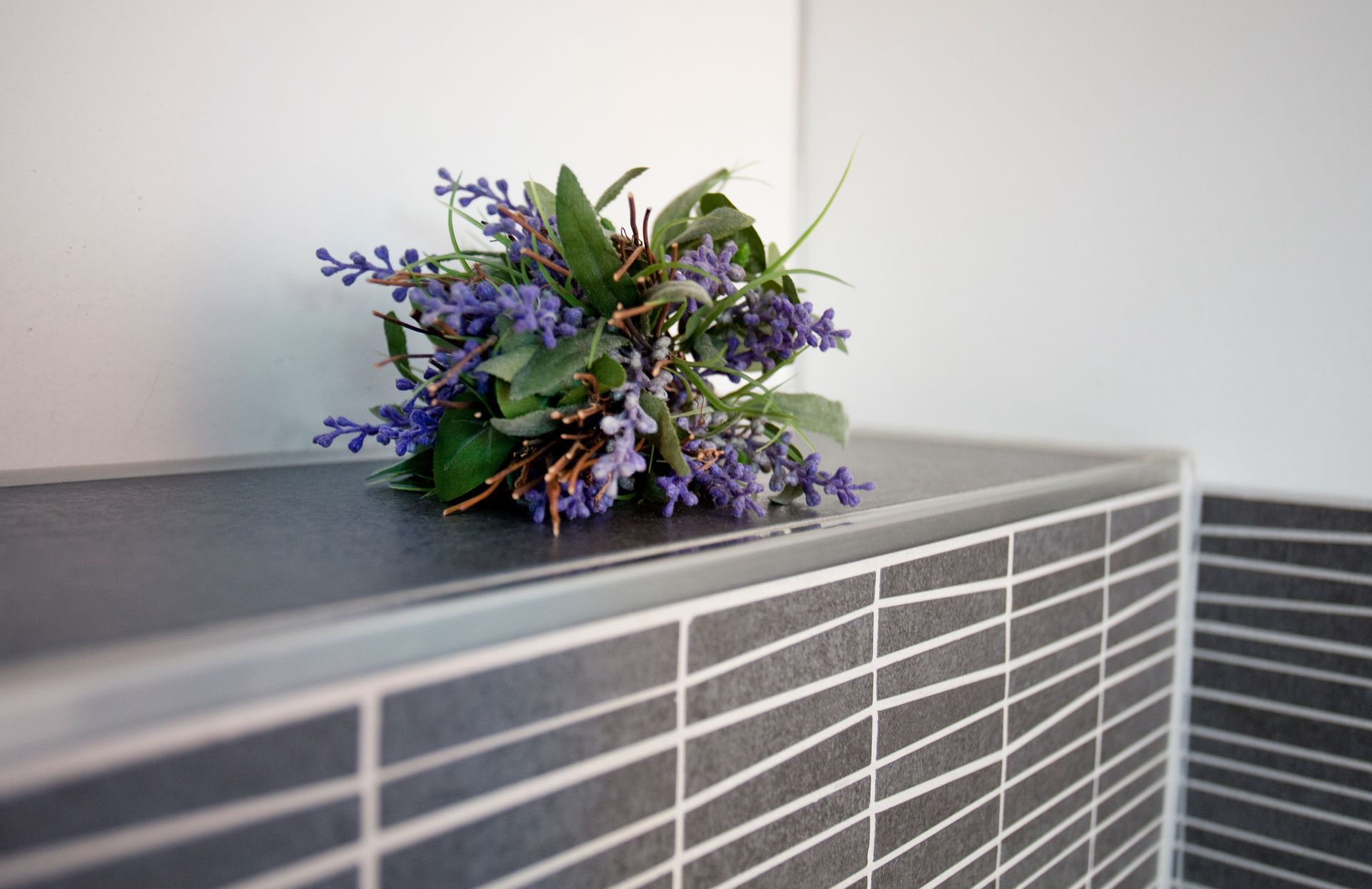 Detailaufnahme einer gefliesten Ablage mit Blumenarrangement.