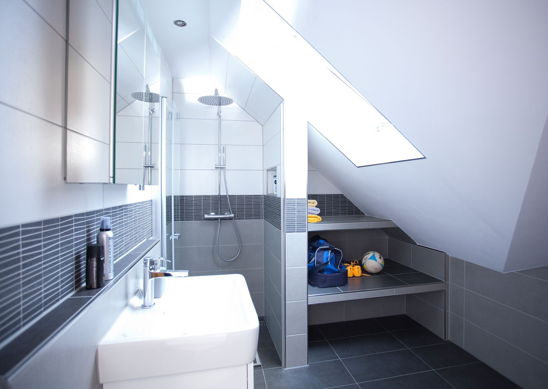 Modernes Bad unter dem Dach mit Dusche, Waschbereich und grauer Fliesenoptik.