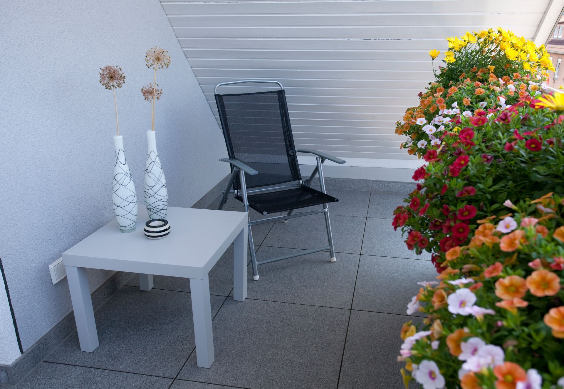 Barrierefrei gestalteter Balkon mit weißem Tisch, Stuhl und Blumenarrangements.