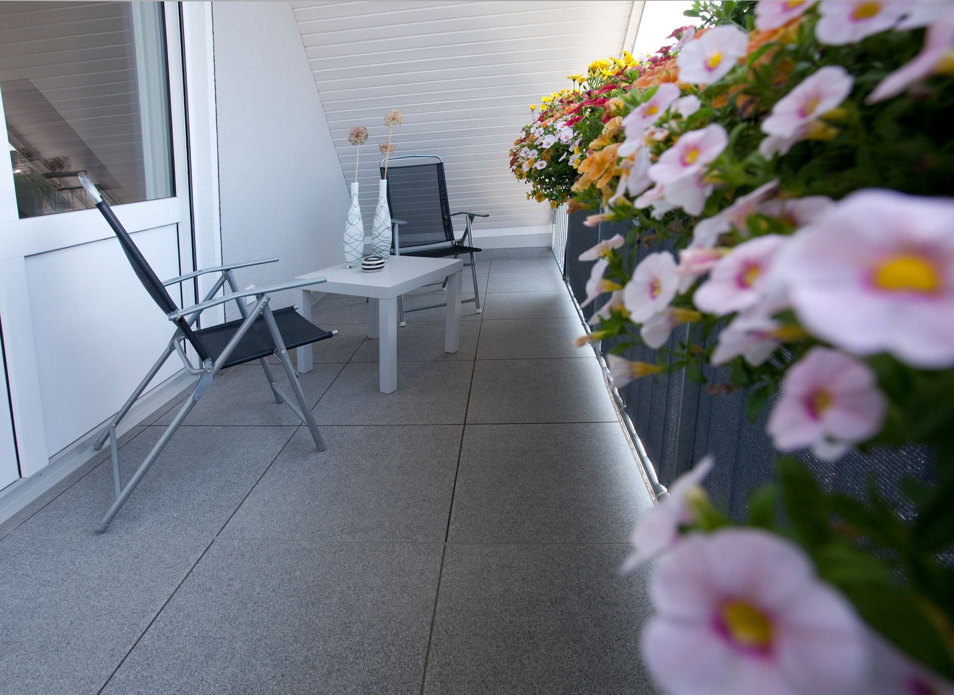 Überdachter Balkon mit rutschfesten Bodenfliesen und Sitzmöbeln.