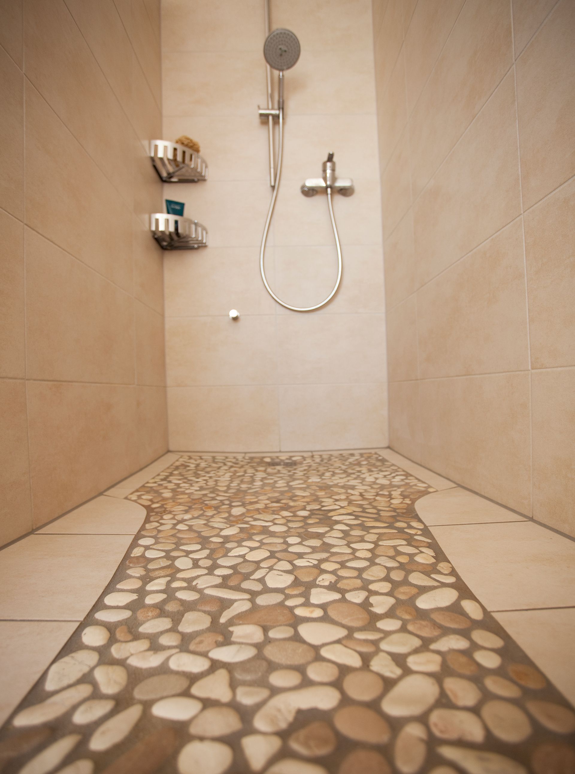 Ebenerdige Dusche mit beigen Wandfliesen und natursteinartigem Kieselmosaik am Boden.