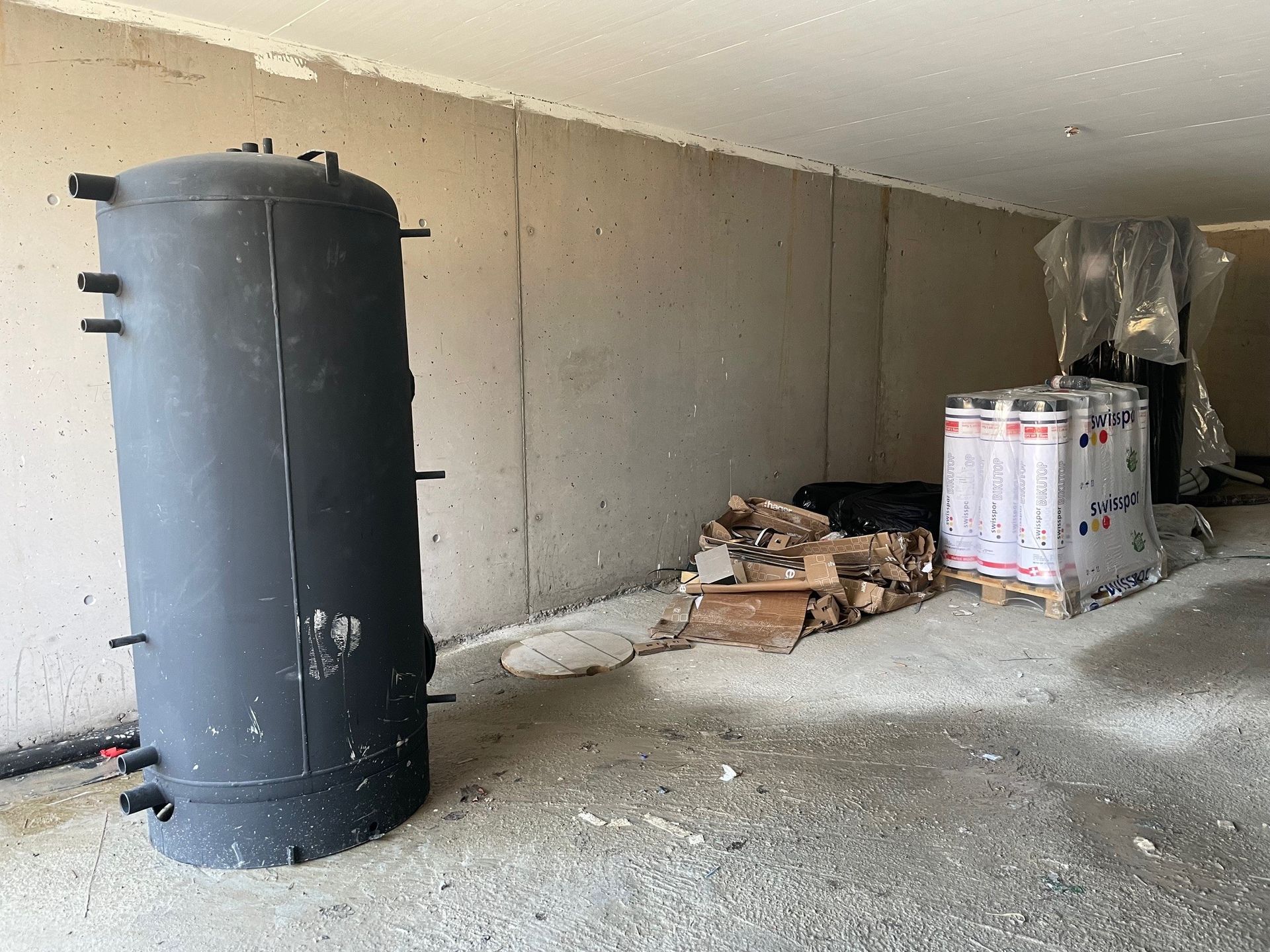 Ein großer schwarzer Tank steht in einem Raum neben einem Holzstapel.