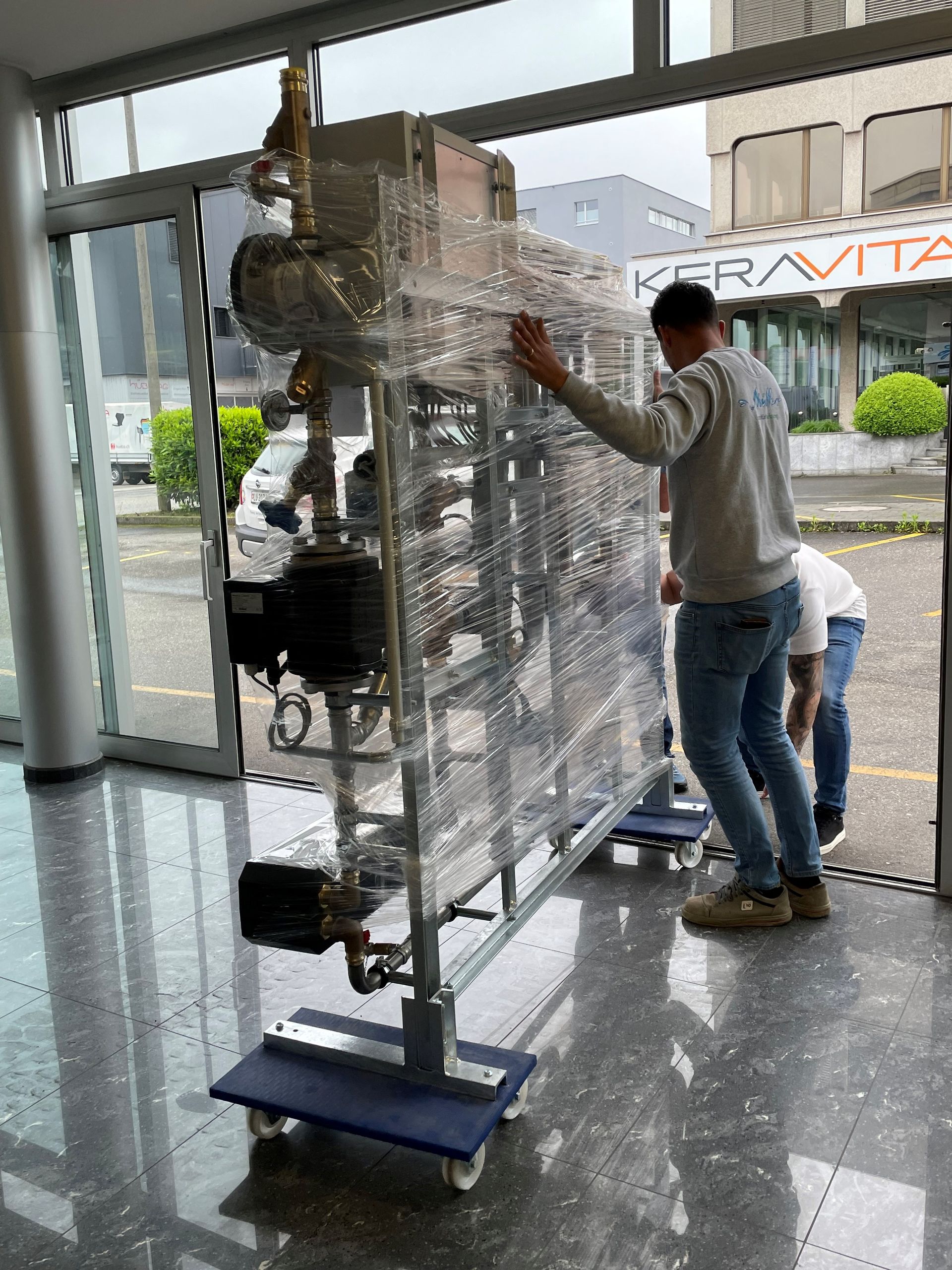 Zwei Männer bewegen ein großes Gerät in einem Raum.