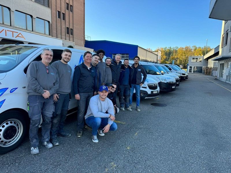 Eine Gruppe von Männern posiert vor einer Reihe von Lieferwagen für ein Foto.