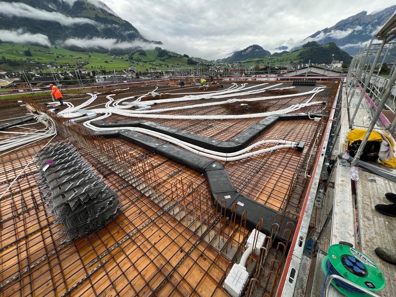 Eine Baustelle mit vielen herausführenden Leitungen und Bergen im Hintergrund.