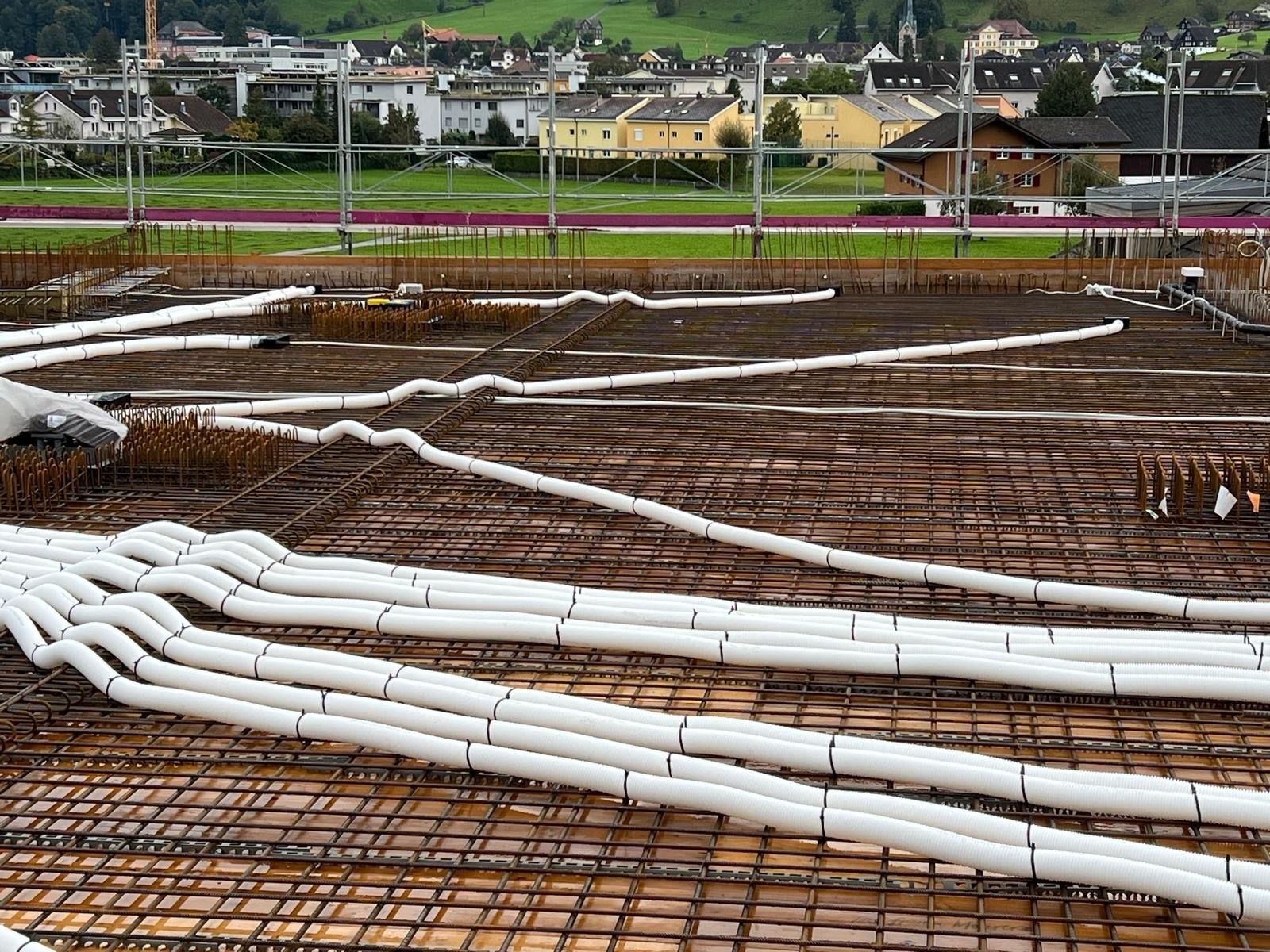 Auf einer Baustelle liegen mehrere weiße Rohre auf dem Boden.