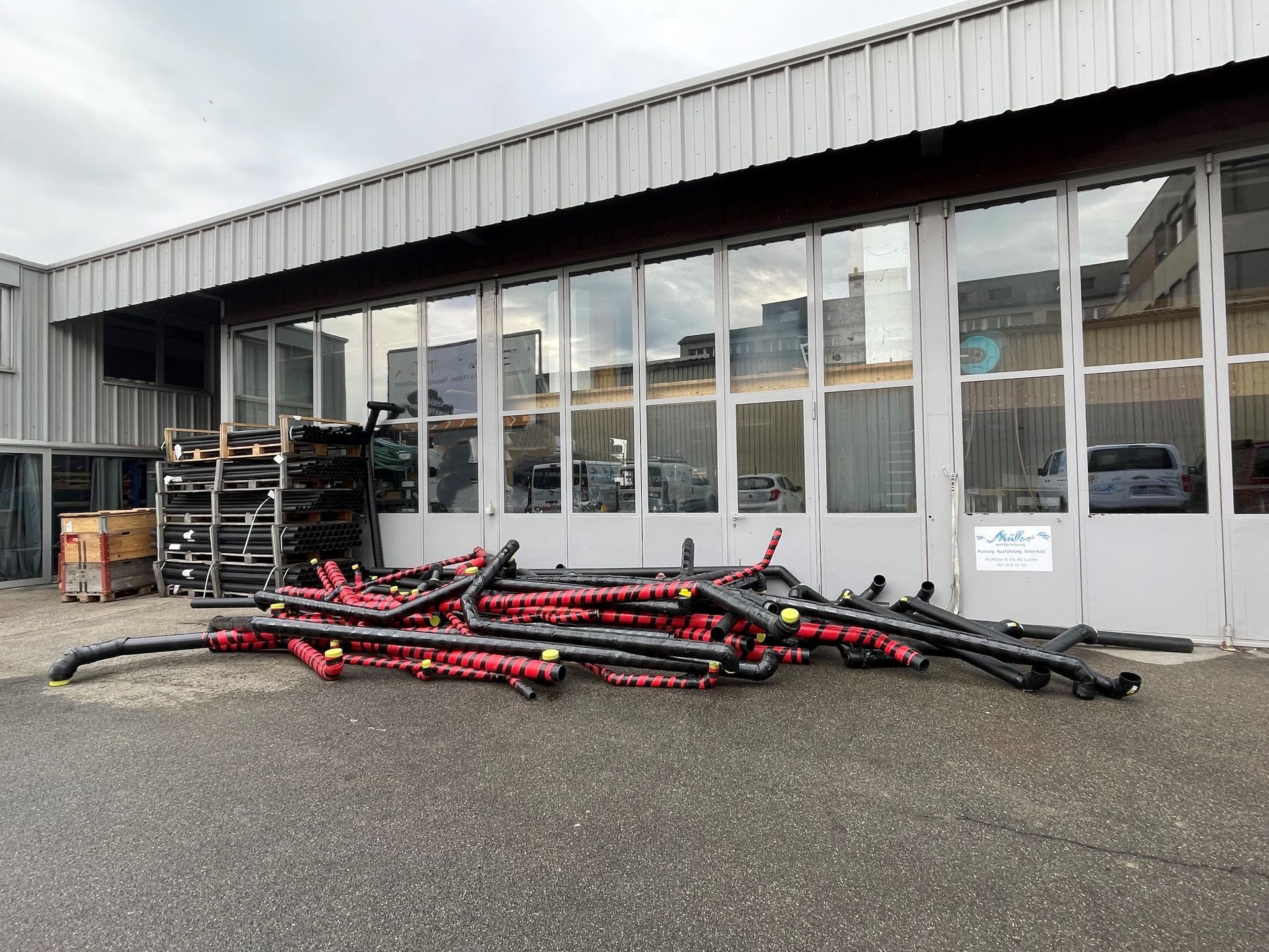 Vor einem Gebäude liegt ein Stapel roter und schwarzer Rohre.