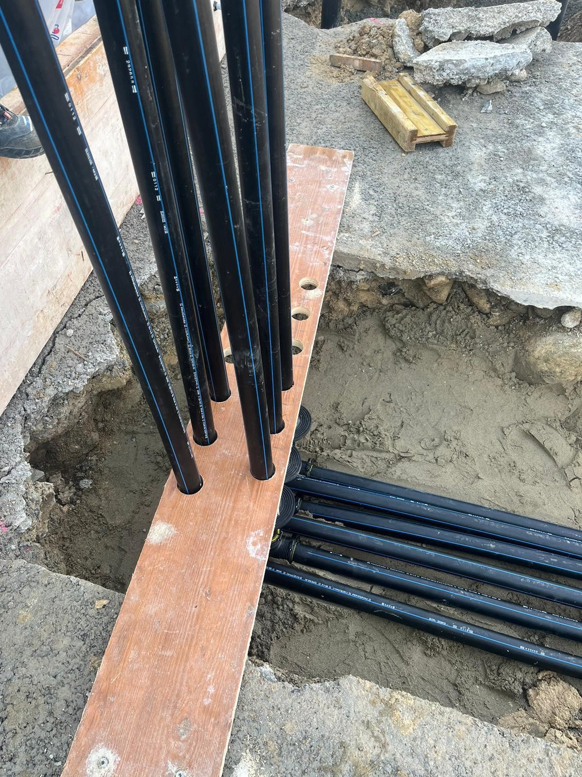 Ein Haufen Rohre liegt auf einem Holzbrett im Dreck.