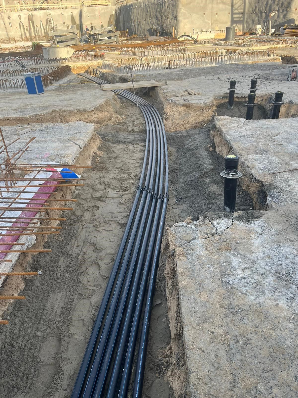 Auf einer Baustelle liegen mehrere schwarze Rohre im Dreck.