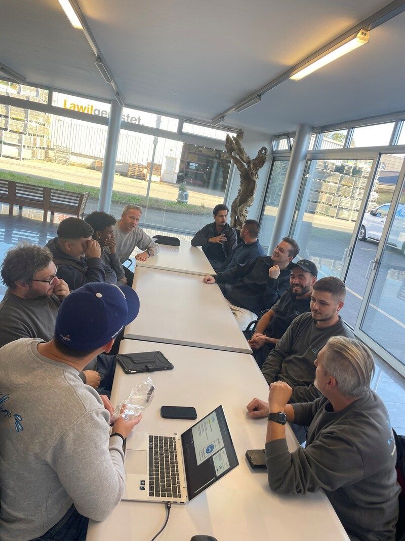 Eine Gruppe Männer sitzt mit Laptops um einen langen Tisch.