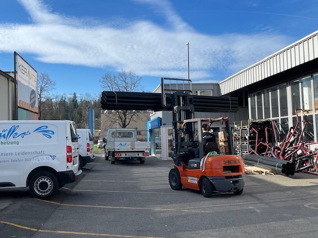 Ein Gabelstapler transportiert ein großes Rohr auf einen Parkplatz.