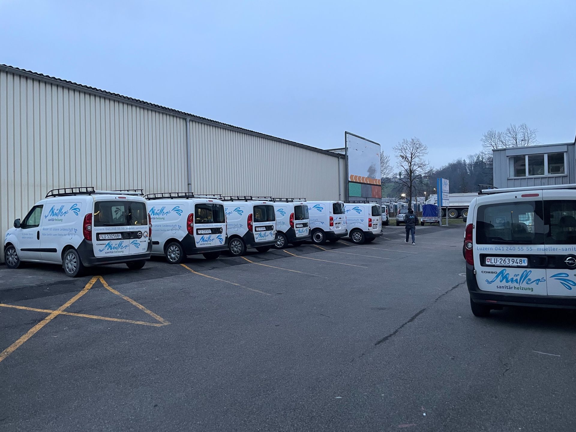 Eine Reihe weißer Lieferwagen steht auf einem Parkplatz vor einem Gebäude.