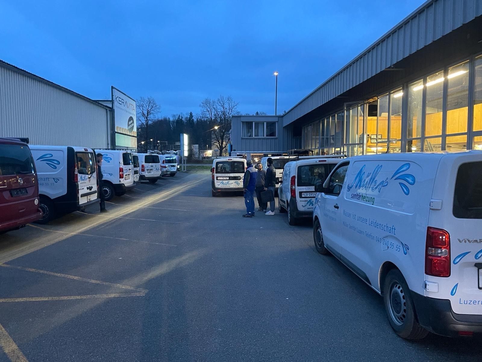Eine Reihe weißer Lieferwagen steht auf einem Parkplatz vor einem Gebäude.